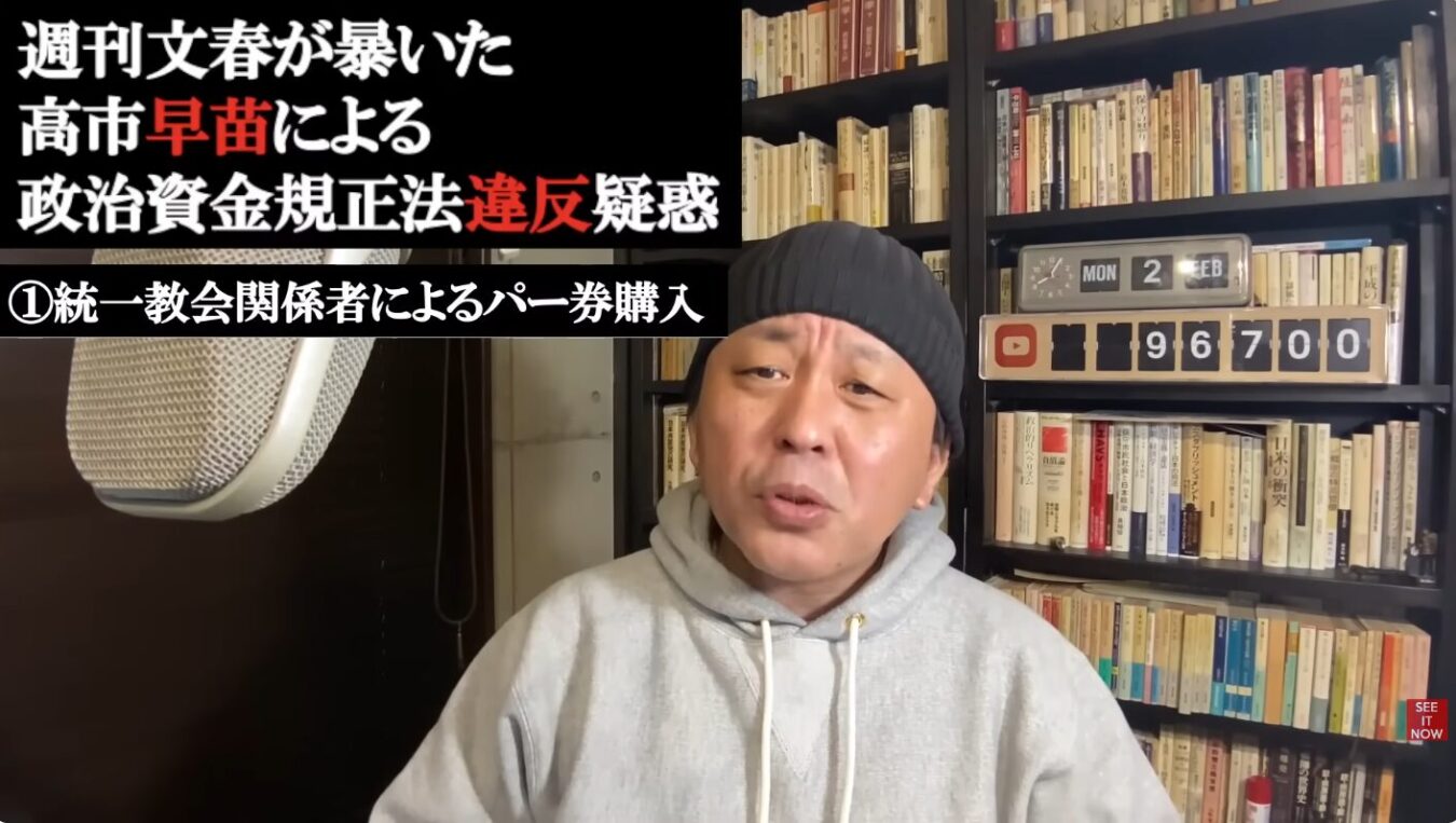 本棚の前でグレーのパーカーと黒いニット帽を着用した菅野完が話しており、画面左上に「週刊文春が暴いた高市早苗による政治資金規正法違反疑惑 ①統一教会関係者によるパー券購入」というテキストが表示されています。