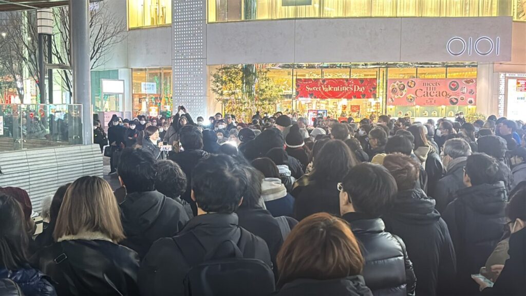 バレンタインの装飾が施された商業施設前の広場に、イベントやパフォーマンスを見ようと大勢の観客が集まっている様子。