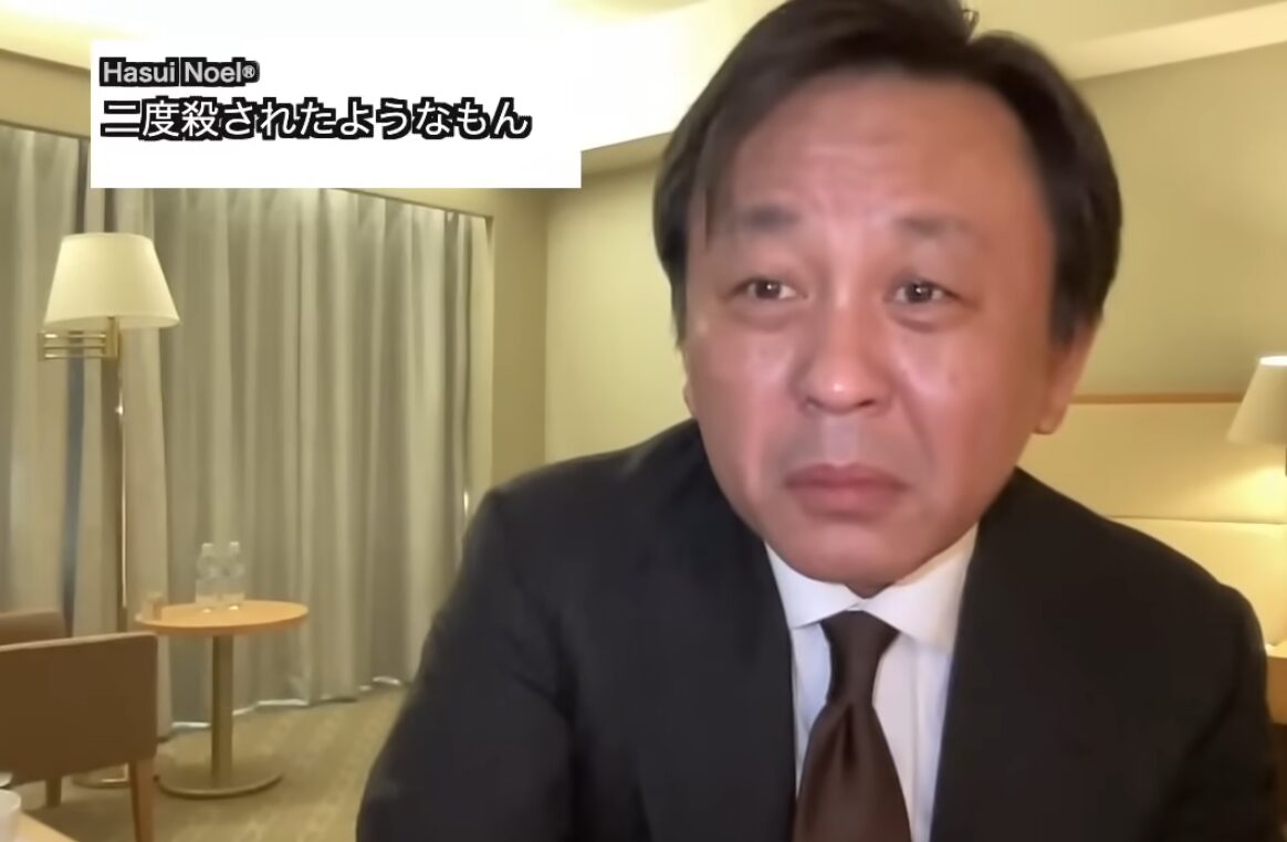 スーツを着た菅野完が、明るい室内で深刻な表情で語りかけており、画面左上に「Hasui Noel® 二度殺されたようなもん」という字幕が表示されている。