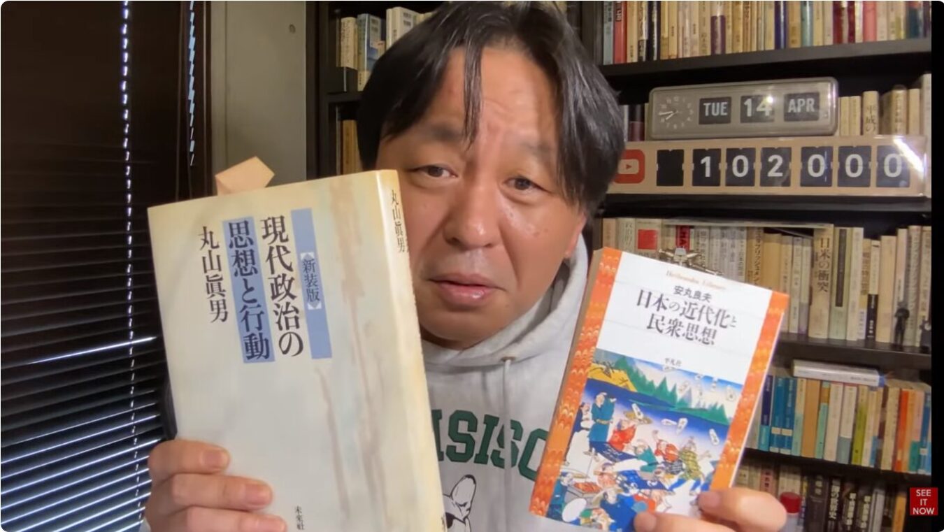 丸山眞男の著書『現代政治の思想と行動』と安丸良夫の著書『日本の近代化と民衆思想』を両手に持って正面を見つめる菅野完。