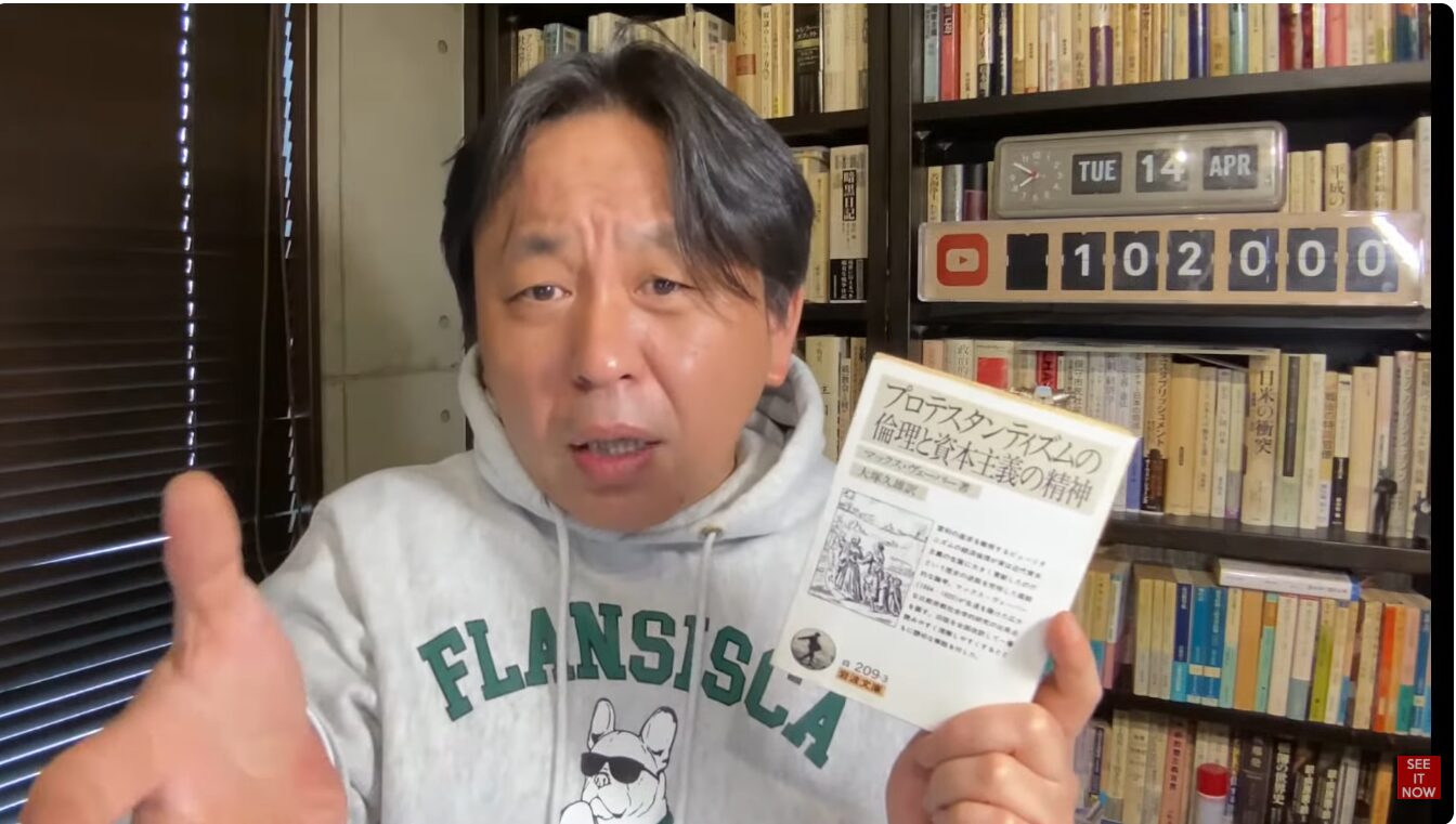 本棚を背景に、マックス・ヴェーバー著『プロテスタンティズムの倫理と資本主義の精神』の文庫本を手に持ち、語りかける菅野完。
