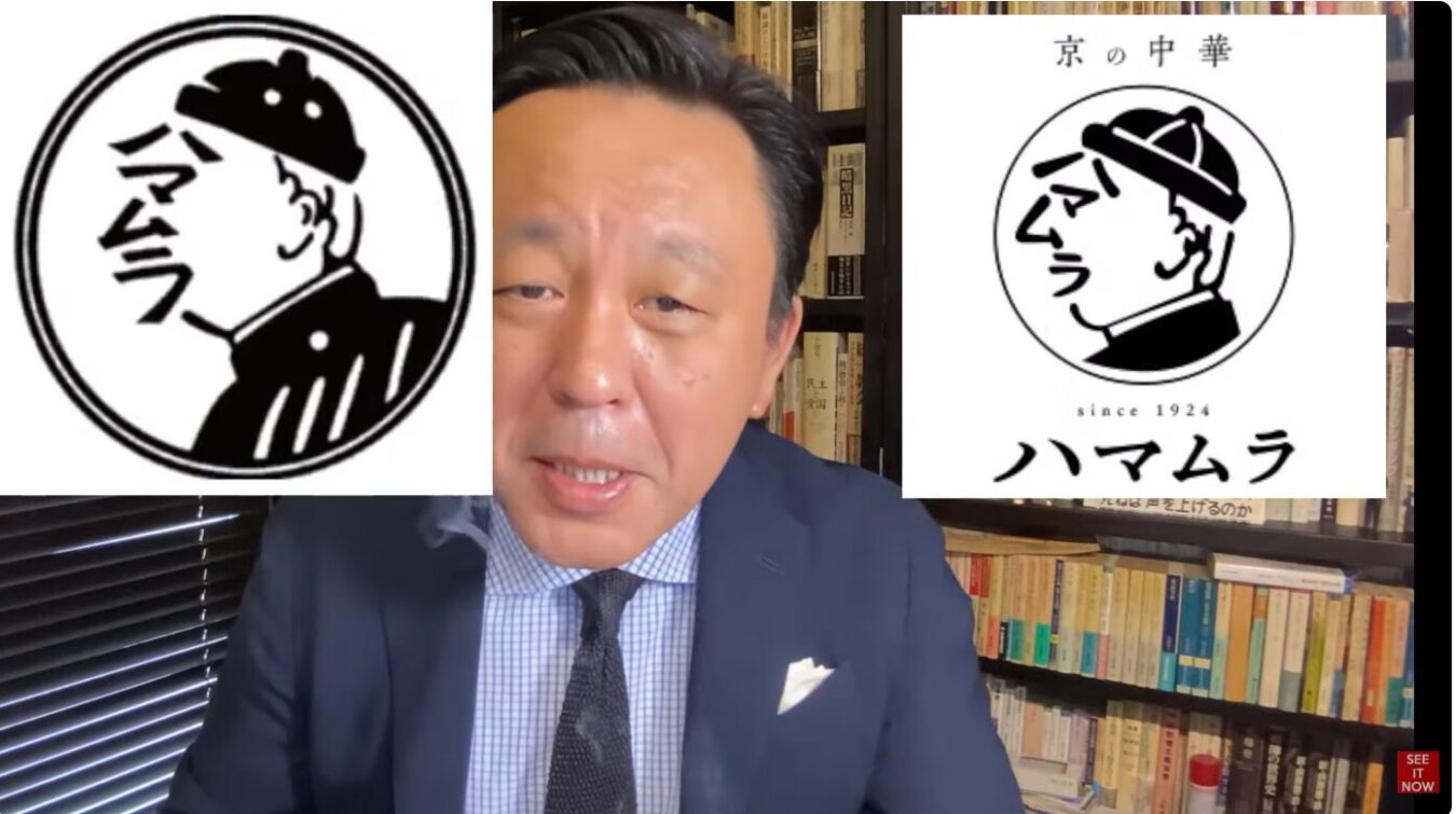 スーツ姿の菅野完の背後に、京都の老舗中華料理店「ハマムラ」のロゴマークが左右に配置されている様子。