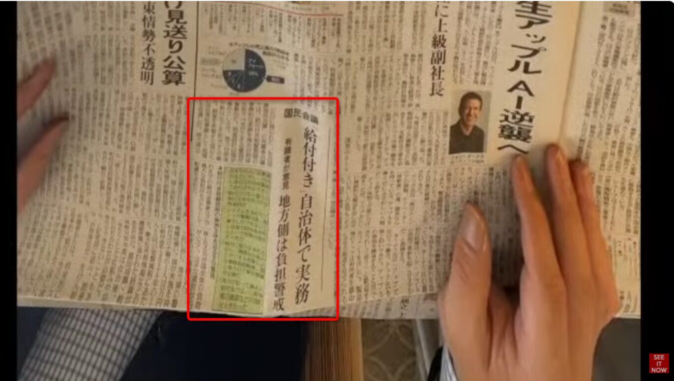 新聞の見出しを指で押さえている手元。