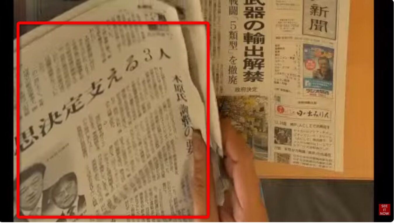 手で持った新聞の紙面を写しており、左側のページには「意思決定支える3人」という見出しと人物写真、右側のページには「武器の輸出解禁」という見出しが掲載されています。