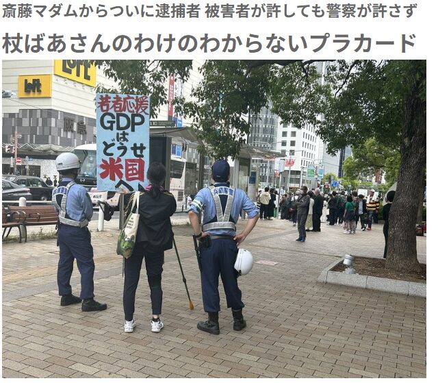 駅前広場で、警察官2人に挟まれて「若者応援 GDPは どうせ米国へ」と書かれたプラカードを掲げる杖を持った女性。