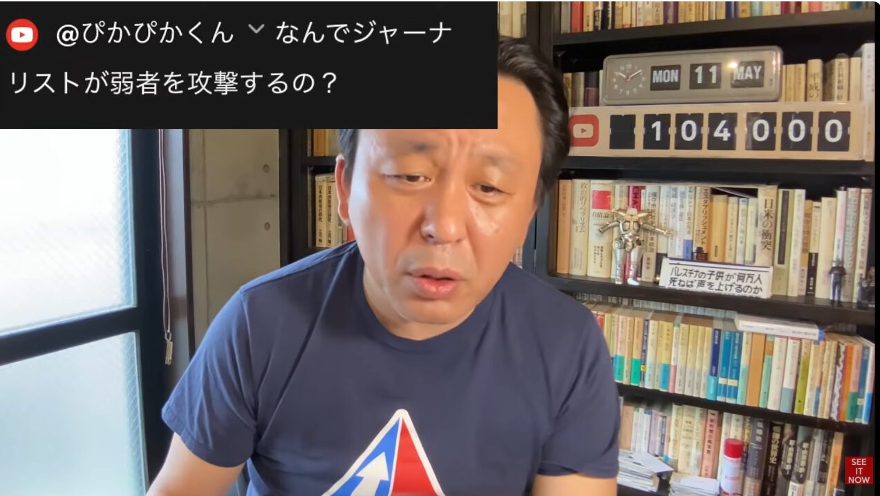 本棚を背景に、YouTubeの視聴者からのなぜジャーナリストが弱者を攻撃するのかという質問コメントを表示し、カメラに向かって話す菅野完。