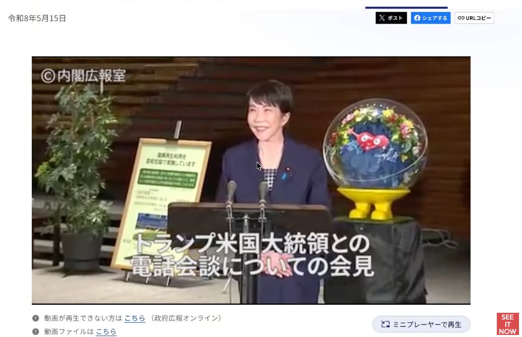 高市早苗大臣がトランプ米国大統領との電話会談についての会見を行い、隣にはEXPO2025大阪・関西万博のキャラクターミャクミャクの花飾りが置かれている。