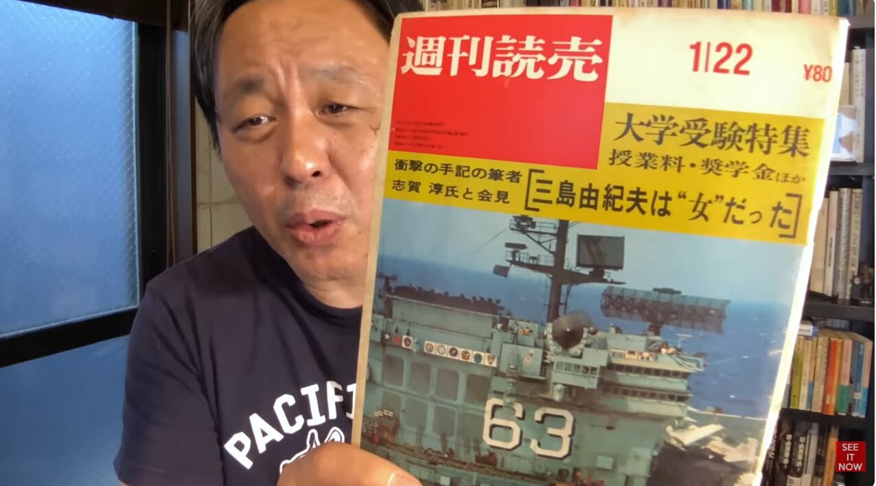 菅野完が週刊読売1月22日号を掲げている。表紙には大学受験特集や三島由紀夫は“女”だったという見出しと、艦番号63の軍艦が写っている。