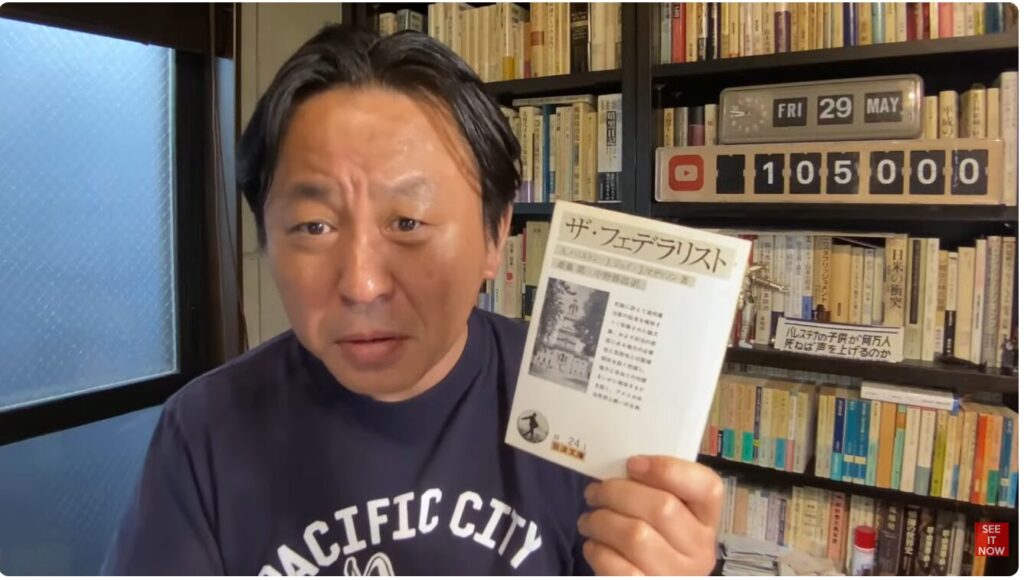 書棚を背に、岩波文庫『ザ・フェデラリスト』を手に持ち、カメラに向かって語りかける菅野完。