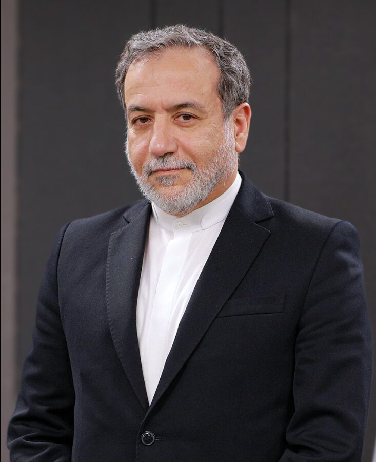 黒のスーツに白のシャツを着用し、あごひげを蓄えた中年のアラグチ外相が、真剣な表情で正面を見つめている様子。