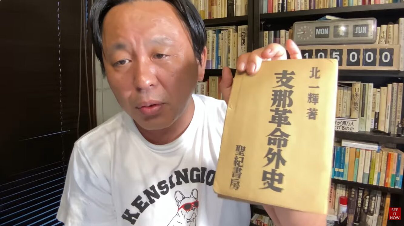 書棚を背にした菅野完が、北一輝著『支那革命外史』(聖紀書房)を手に持ち、紹介している様子。