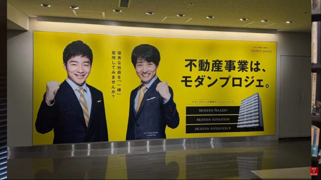不動産事業は、モダンプロジェ。のコピーと、スーツ姿でポーズをとるジャルジャルが描かれた黄色の広告。