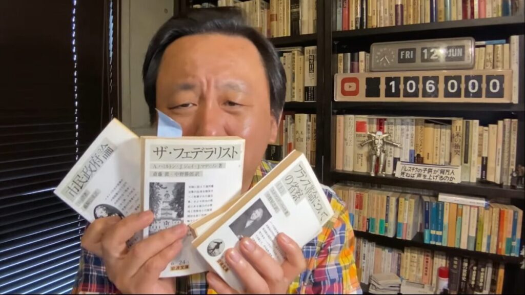 本棚を背景に、菅野完が『市民政府論』『ザ・フェデラリスト』『フランス革命についての省察』の3冊の文庫本を掲げている。