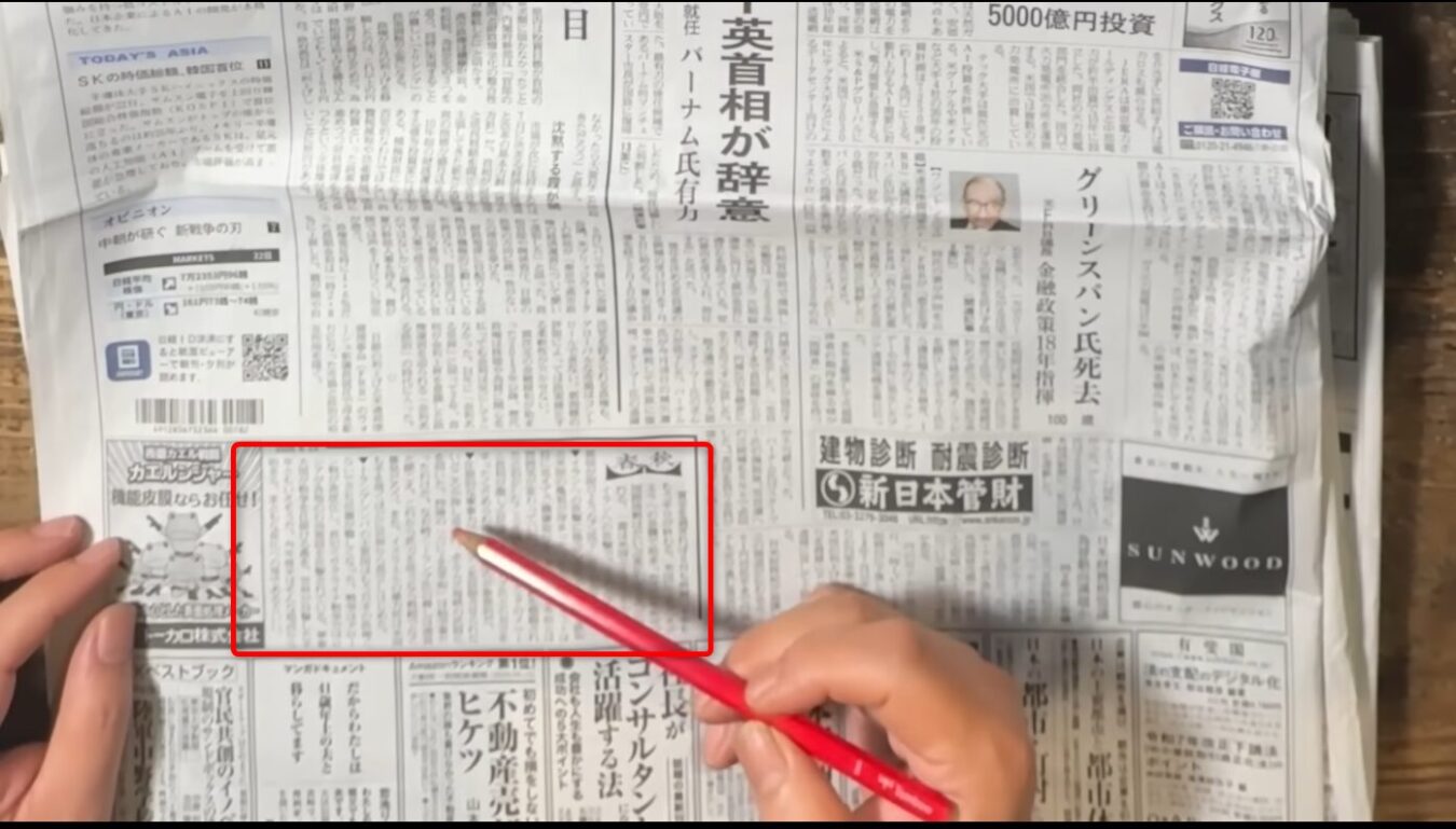 手にした赤いペンで、日本経済新聞のコラム春秋の一節を指し示しながら読んでいる様子。