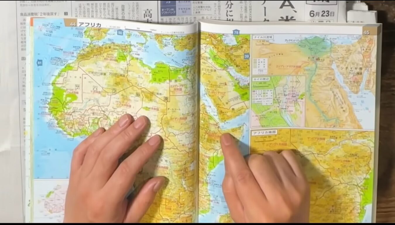 開いた地図帳のアフリカ大陸のページを両手で指差しながら確認している様子。