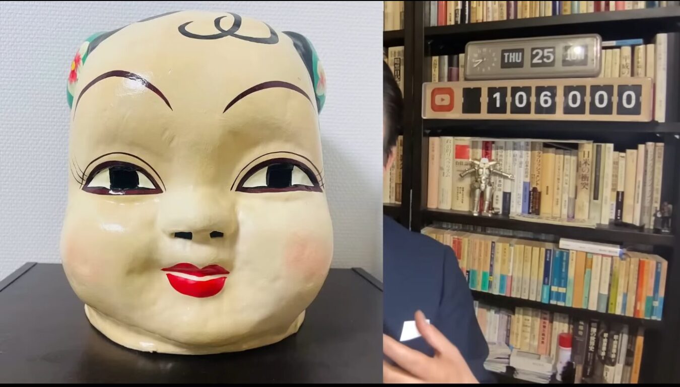 左側に置かれた大きな中国風の子供の仮面と、右側にある本棚や登録者数カウンターなどの室内風景。