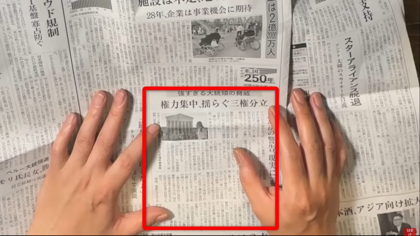 権力集中、揺らぐ三権分立という見出しと最高裁判所庁舎のモノクロ写真が掲載された新聞記事を両手で広げている様子。