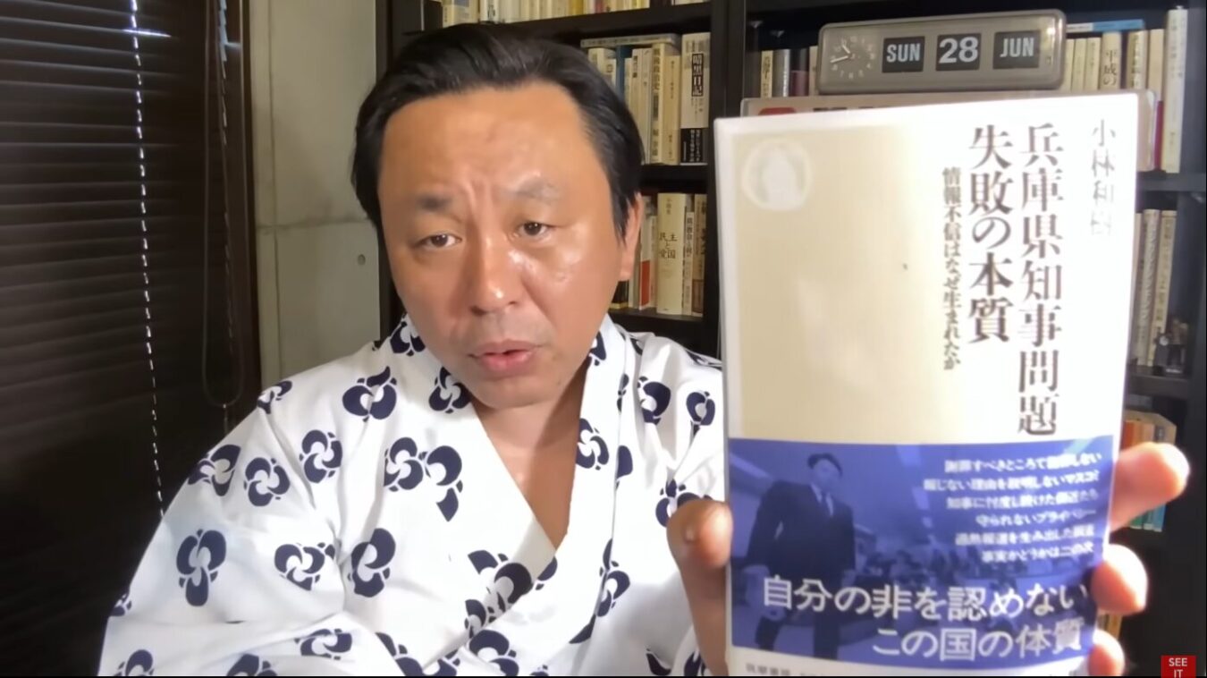 浴衣姿の菅野完が、書籍兵庫県知事問題 失敗の本質を手に持ち、カメラに向けて紹介している場面。