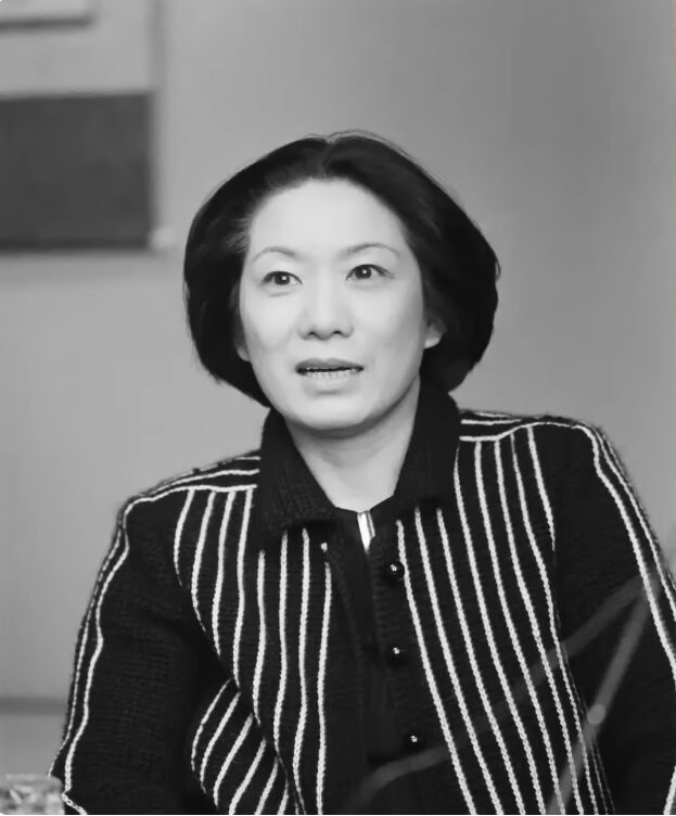 黒と白のストライプ柄のジャケットを着用し、少し口を開けて話をしているショートヘアの向田邦子のモノクロポートレート。