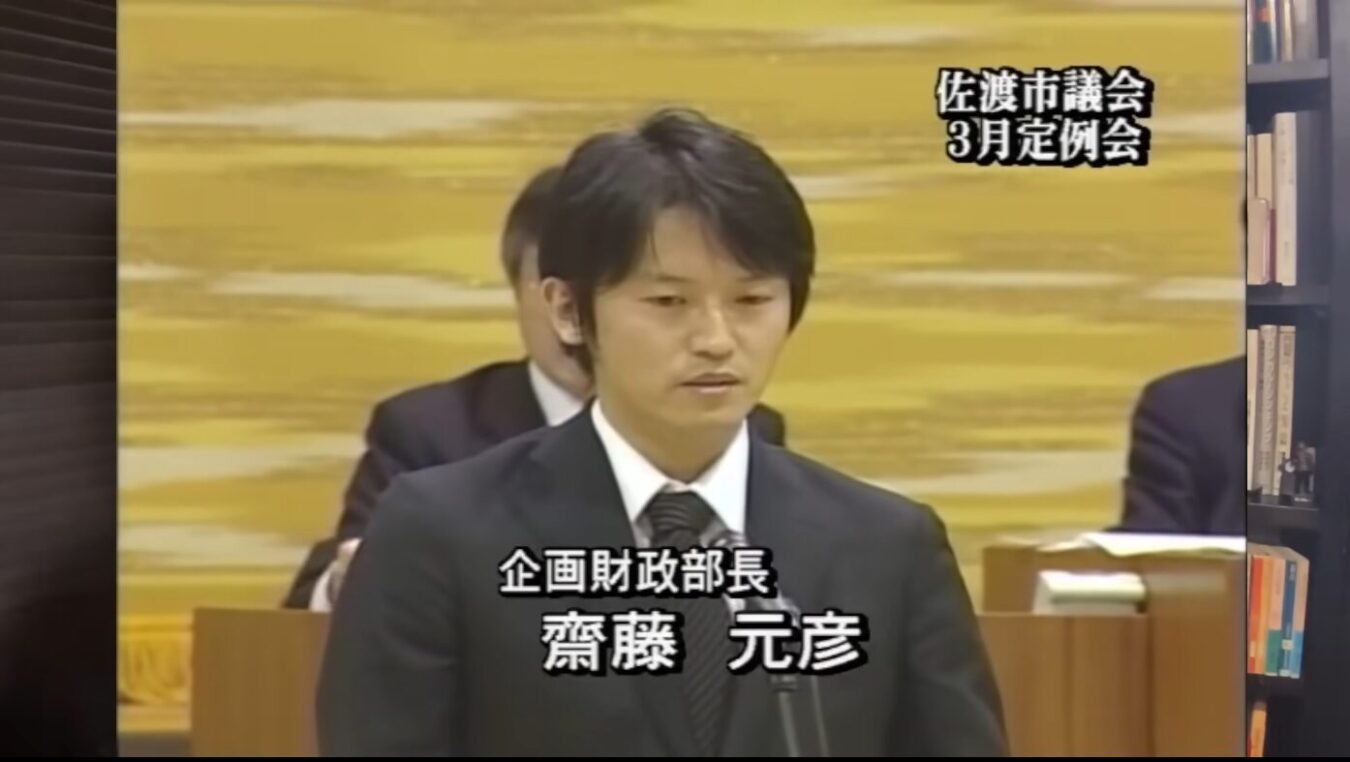 佐渡市議会3月定例会において、企画財政部長として答弁に立つスーツ姿の齋藤元彦氏。