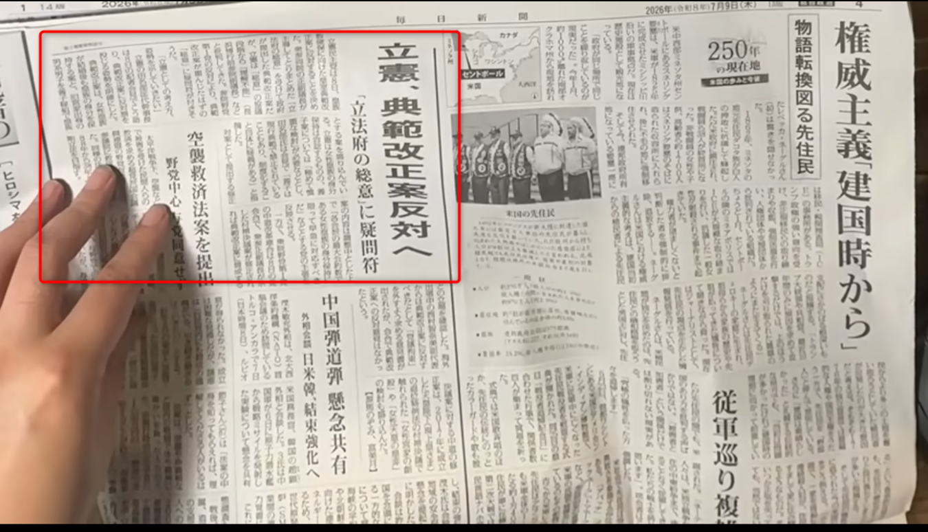 新聞紙面の一面を左手の指先が押さえている様子