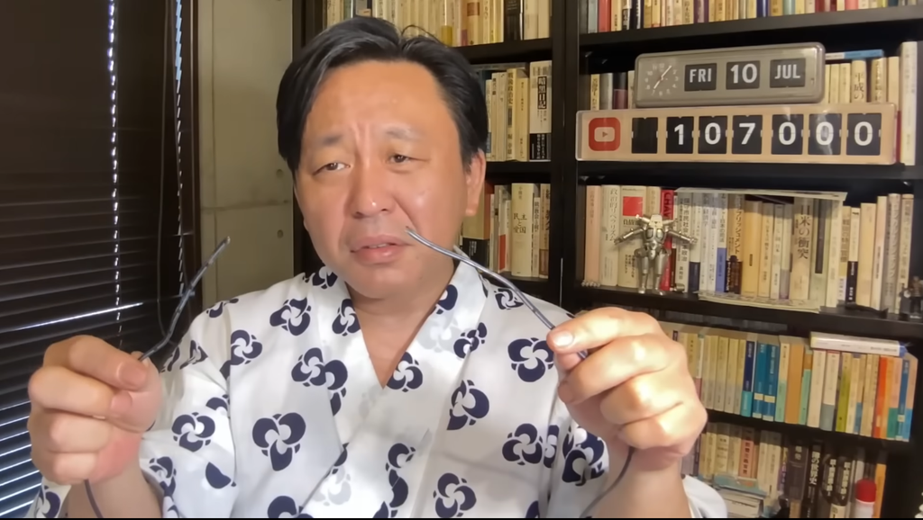 浴衣を着て両手に千切れたメガネを持っている菅野完
