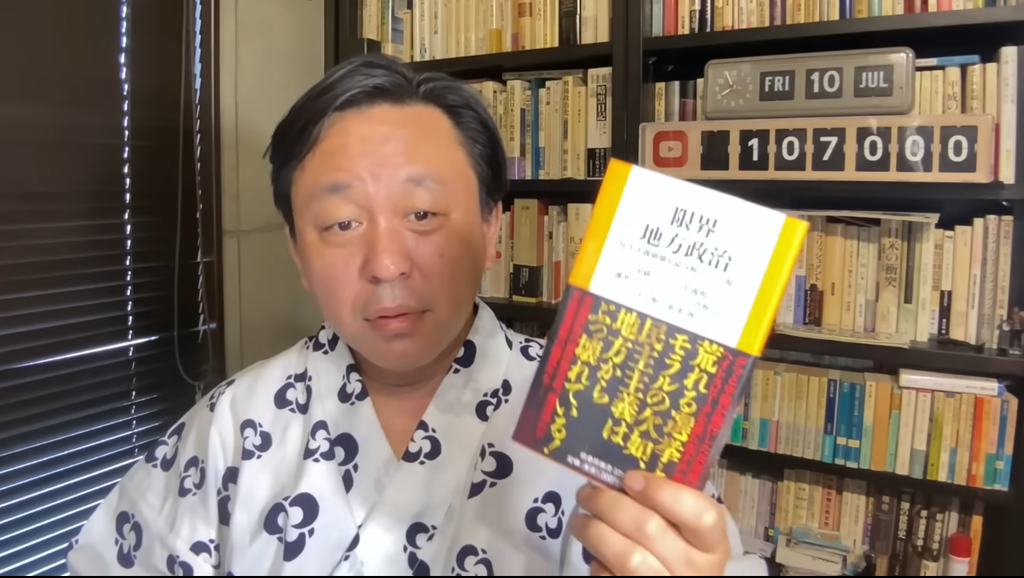 浴衣姿の菅野完が「限界地方政治」というタイトルの本を手に持ってカメラに向かって話している画像