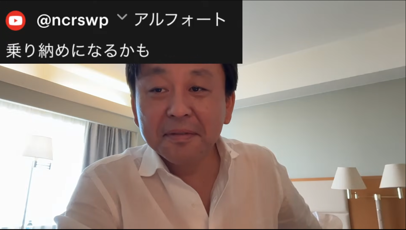 白いシャツを着て室内で話をする男性のバストショット、左上にYouTubeチャンネル風のテキストが表示されている。