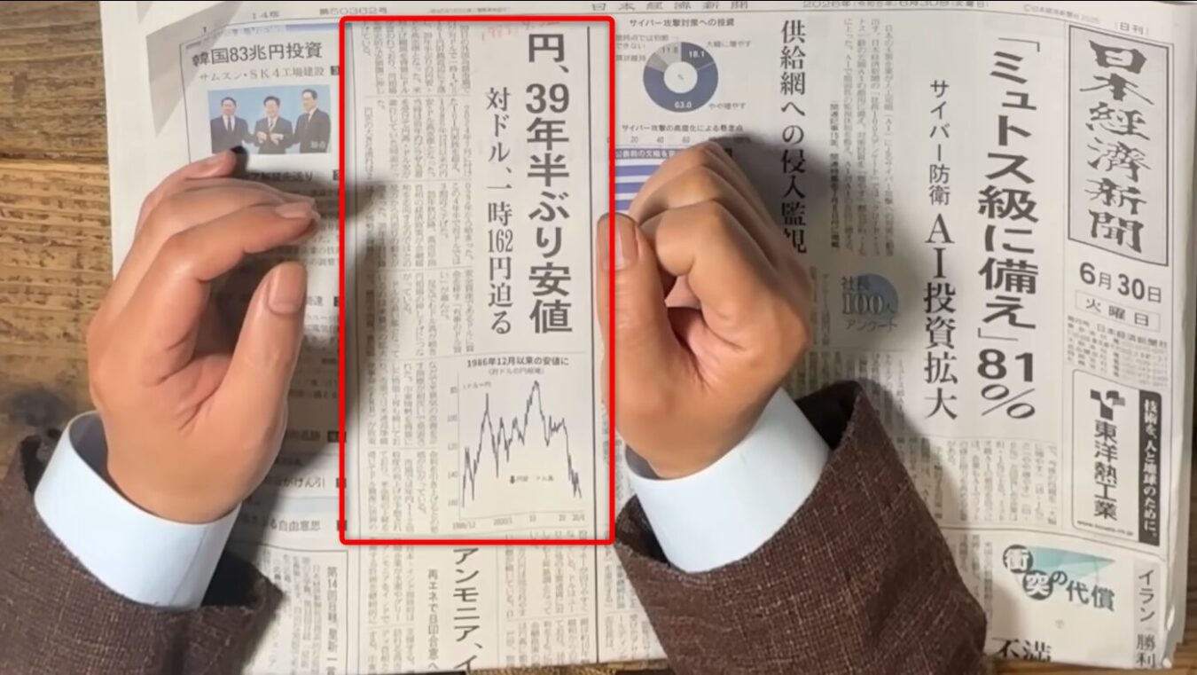 円安の進行を報じる日本経済新聞の記事と、その内容を指し示す人物の手元が写っている様子。