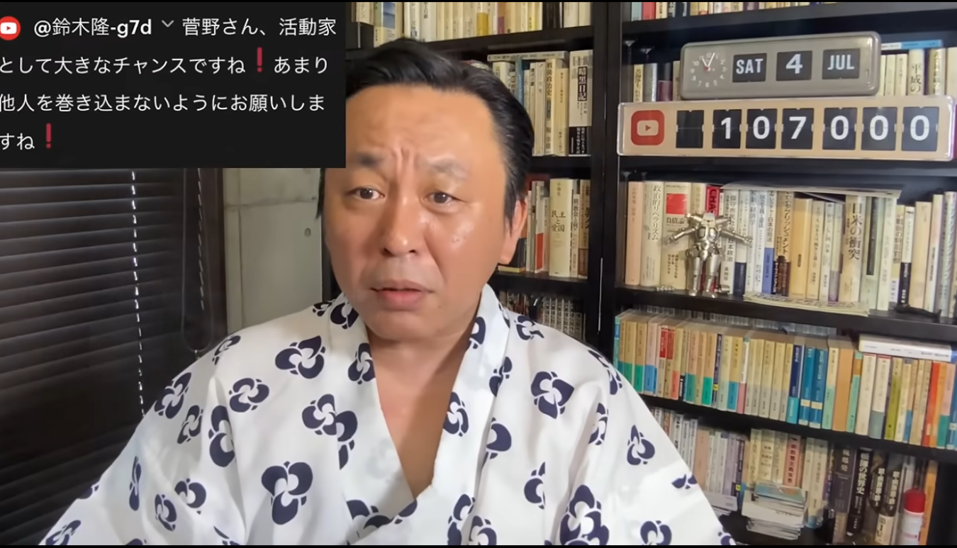 浴衣を着て本棚の前に座り、カメラに向かって話す男性。背景には日付と登録者数が表示されたデジタル時計がある。