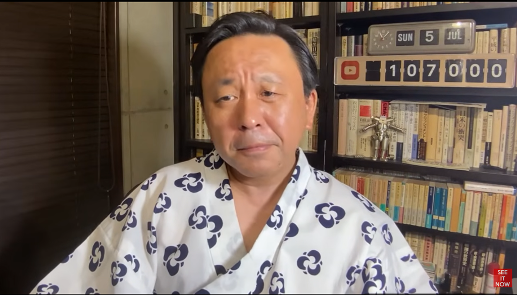 浴衣を着て本棚の前に座り、カメラを見つめる菅野完のポートレート。背景にはYouTubeの登録者数カウンターがある。