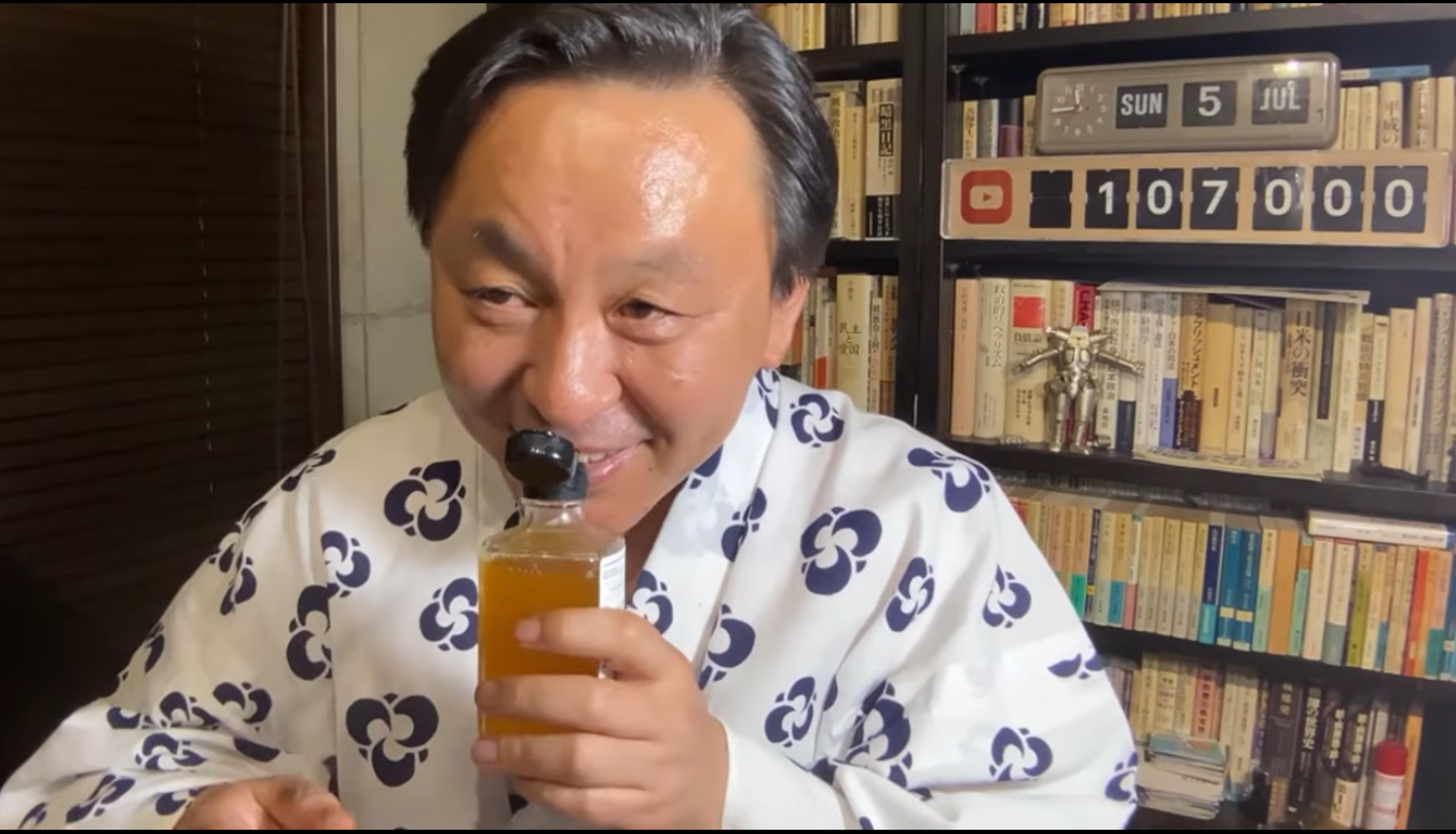 浴衣を着た菅野完が、手にした小瓶の香りを嗅ぎながら微笑んでいる様子。背景には本棚とYouTubeの登録者数カウンターがある。