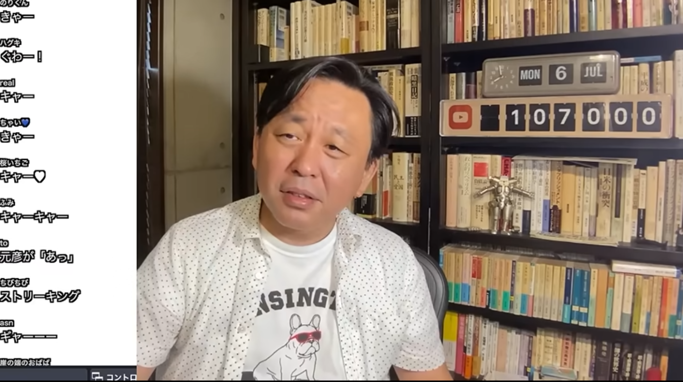 本棚を背景に、白いドット柄のシャツを着てカメラに向かって話す菅野完のライブ配信の様子。