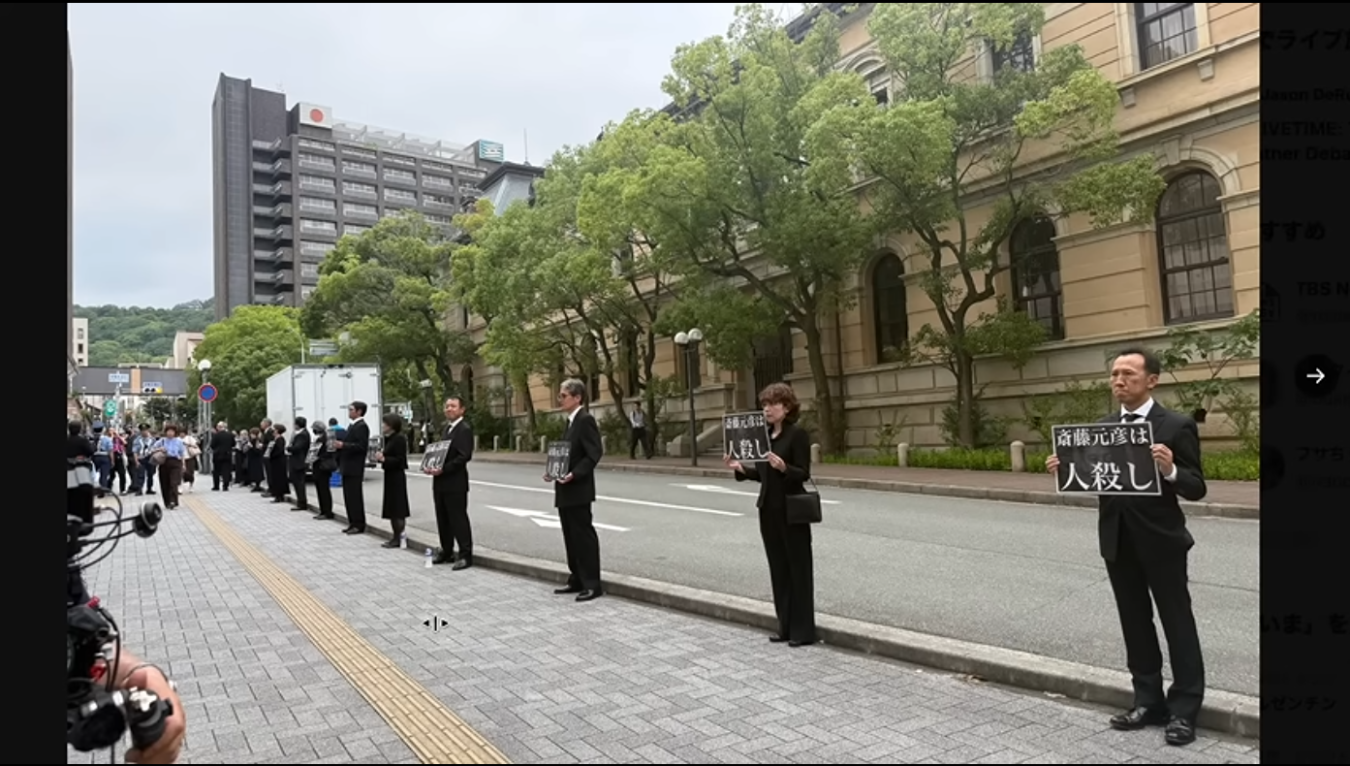 兵庫県庁前で「斎藤元彦は人殺し」と書かれたプラカードを掲げて抗議活動を行う人々の様子。