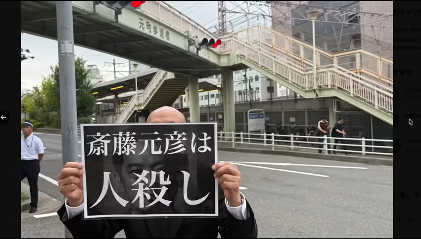 兵庫県知事の斎藤元彦氏を批判する内容が書かれたプラカードを掲げて街頭に立つ男性の様子。