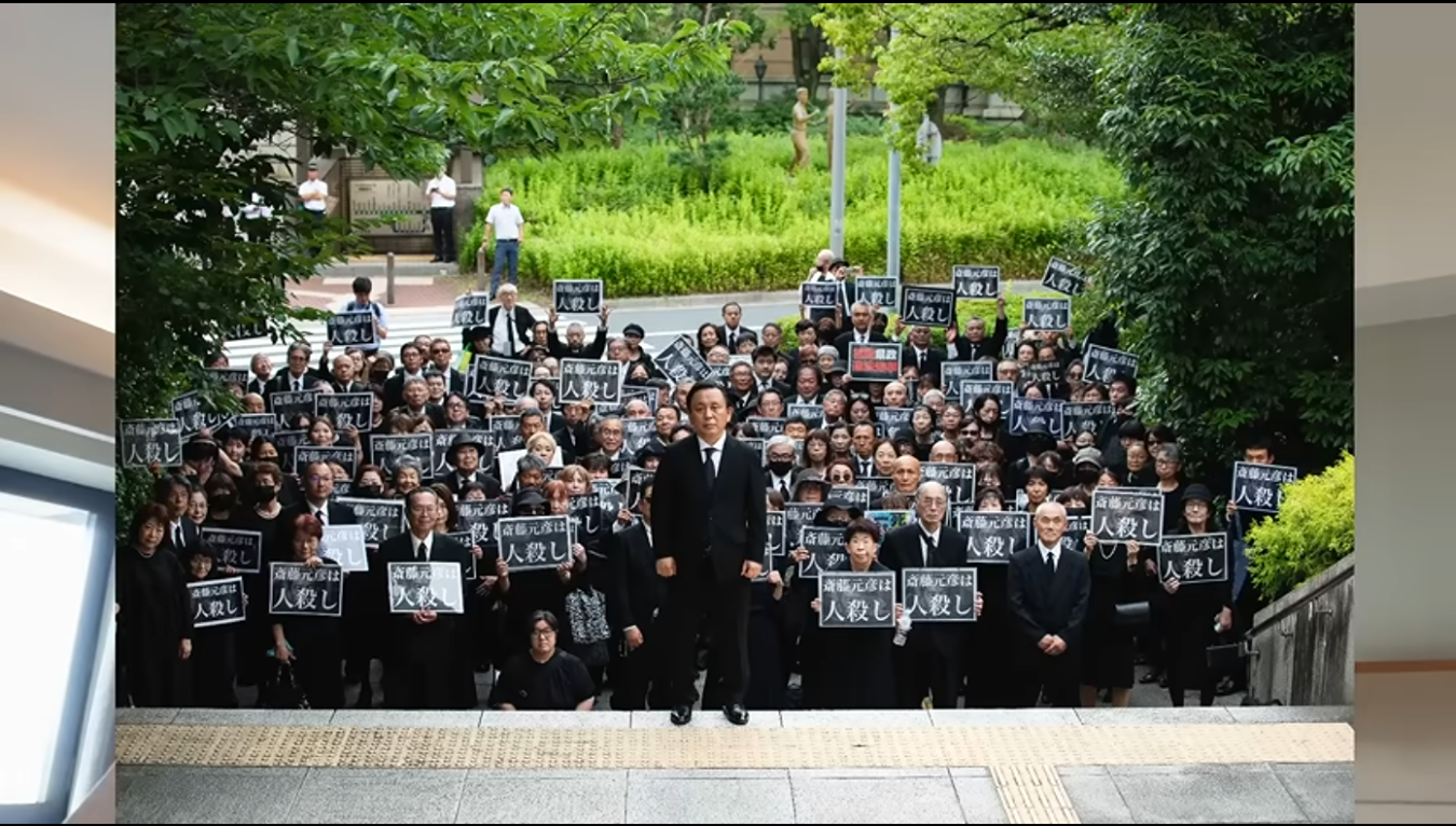 兵庫県庁前で斎藤元彦知事の辞職を求め、黒い喪服姿で「斎藤元彦は人殺し」と書かれたプラカードを掲げる大勢の抗議者たち。