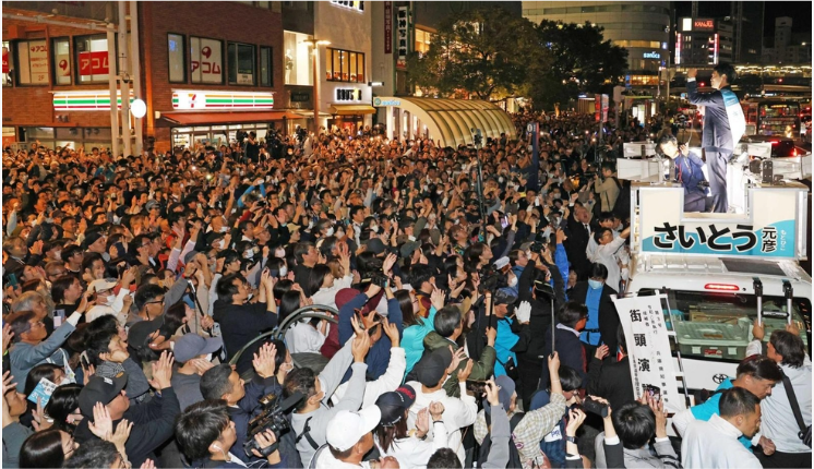 夜間の街頭演説でスピーカー車の上に立ち、集まった大勢の聴衆に手を振る政治家
